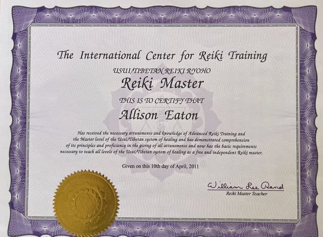 The image contains a certificate that certifies a person as a "Reiki Master" from "The International Center for Reiki Training." It includes the person's name, states their achievement in attaining necessary knowledge and proficiency in Reiki training, and mentions the date of issuance as April 10, 2011. The certificate features a seal or emblem in gold at the bottom left and is decorated with a purple border. The signature of a person identified as a "Reiki Master Teacher" is present at the bottom.