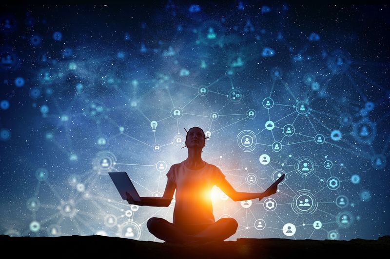 The image depicts a person sitting in a meditative pose against a dark, starry background. The individual is holding a laptop in one hand and appears to be engaged in some form of contemplation or concentration. Surrounding the figure are various graphic elements that suggest a connection to digital networks or social media, including icons and interconnected lines, creating a sense of a technological or virtual environment. The overall composition gives a feeling of harmony between technology and meditation.