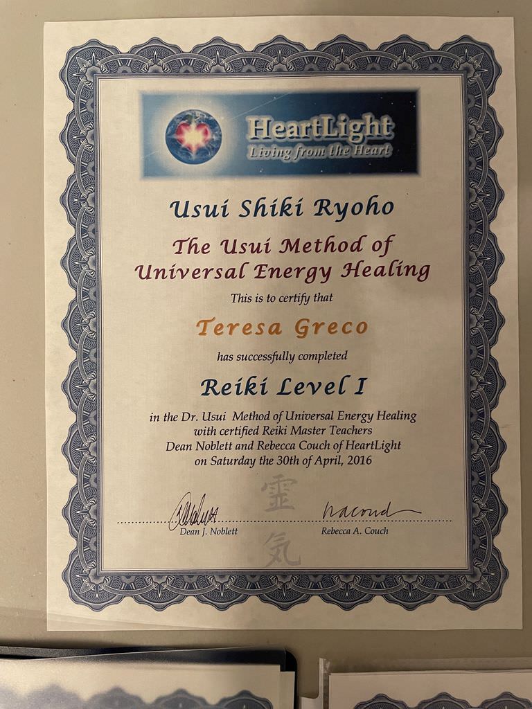 The image is a certificate that certifies the completion of Reiki Level I training. It features the following elements:

1. A logo at the top that says "HeartLight" along with the phrase "Living from the Heart."
2. The title "Usui Shiki Ryoho" and "The Usui Method of Universal Energy Healing."
3. A statement confirming the certification of an individual, indicating successful completion of the course.
4. The name "Teresa Greco" is mentioned as the person who completed the training.
5. The certificate is signed by two individuals, Dean Noblett and Rebecca Couch, and includes a date: April 30, 2016.
6. The border design is ornate, with decorative elements around the edges. 

Overall, it is a formal document acknowledging someone's training in Reiki healing.