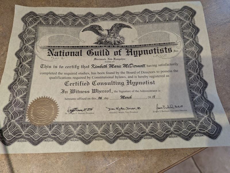 The image shows a certificate from the National Guild of Hypnotists, issued in New Hampshire. It certifies that an individual has satisfactorily completed the required studies and is registered as a Certified Consulting Hypnotist. The certificate features decorative elements, including an eagle emblem and an official seal. It is dated March 2018 and includes signatures from officials of the organization.