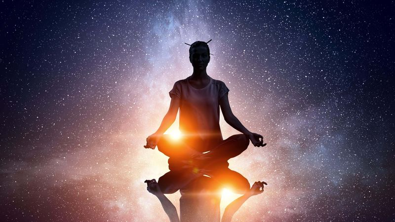 The image depicts a silhouette of a person meditating in a cross-legged position. They are surrounded by a cosmic background featuring stars and a galaxy, with bright light emanating from beneath them, creating a reflective effect. The overall atmosphere conveys a sense of tranquility and connection to the universe.