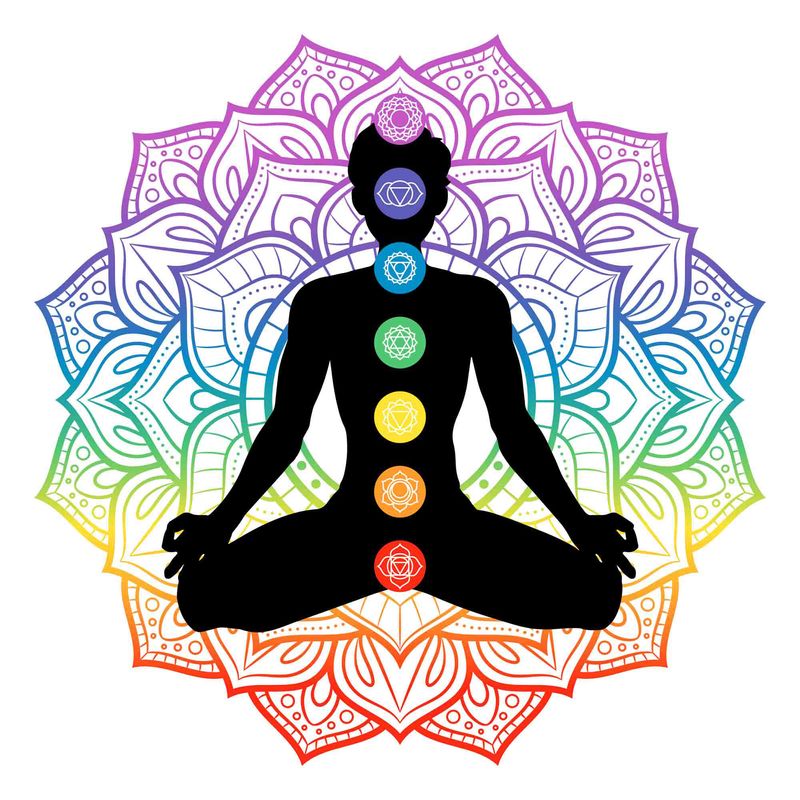 The image depicts a silhouette of a meditating figure seated in a cross-legged position. Behind the figure is a colorful mandala design featuring intricate patterns in a gradient of colors, transitioning from purple at the top to red at the bottom. Along the center of the figure are the seven chakras, represented by colored circles, each with a distinct symbol corresponding to the chakra colors: violet, indigo, blue, green, yellow, orange, and red. The overall theme suggests concepts of spirituality, balance, and energy.