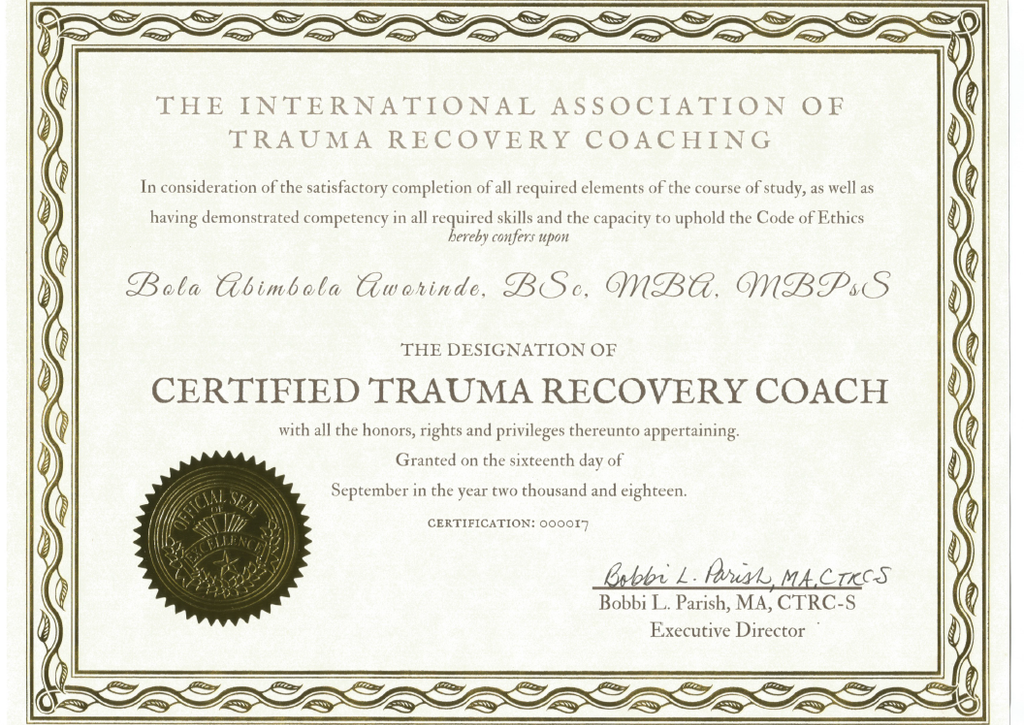 The image is a certificate from the International Association of Trauma Recovery Coaching. It recognizes the completion of required studies and competencies in trauma recovery coaching. The certificate designates the individual as a "Certified Trauma Recovery Coach" and includes the name "Bola Abimbola Awrindé" along with academic titles. It is dated September 16, 2018, and signed by Bobbi L. Parish, the Executive Director. The certificate features decorative borders and a seal.