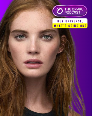 The image features a close-up of a person with long, wavy reddish-brown hair and a natural makeup look. The background is a vibrant purple, and there is text overlay in the corner that appears to be related to a podcast titled "THE ORYKL PODCAST," along with a question that reads, "HEY UNIVERSE, WHAT’S GOING ON?" The overall composition highlights the person's face while incorporating branding for the podcast.