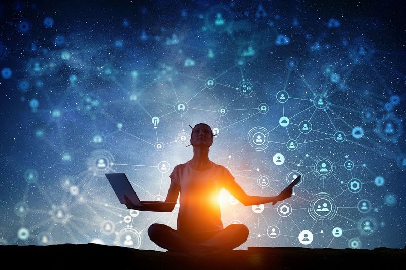 The image depicts a silhouette of a person sitting cross-legged with a laptop in one hand and an outstretched hand, suggesting a state of meditation or mindfulness. The background features a starry night sky with an array of interconnected digital symbols and icons, resembling a network, which suggests themes of technology, connectivity, and possibly data or social media. The bright light emanating from the person's chest adds an element of warmth and illumination to the scene.