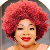 The image features a woman with a vibrant red, curly afro hairstyle. She is smiling and wearing bold red lipstick, along with dangling earrings. Her outfit appears to be a light-colored top, and the background consists of soft, blurred tones that suggest a casual setting. The image is presented in a circular crop.