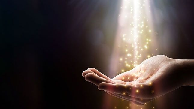 The image features a human hand, palm open and facing upward, against a dark background. Above the hand, there is a beam of light streaming down, which appears to be emanating sparkles or glowing particles, creating a magical or ethereal effect. The overall mood of the image is mystical and enchanting.